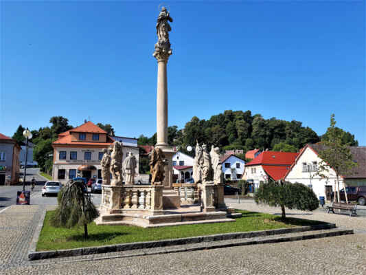 Úpravné náměstí městečka Pecka s morovým sloupem z roku 1720, zakončeným Korintskou hlavicí, na níž stojí socha Panny Marie. V pozadí hotel Koruna.